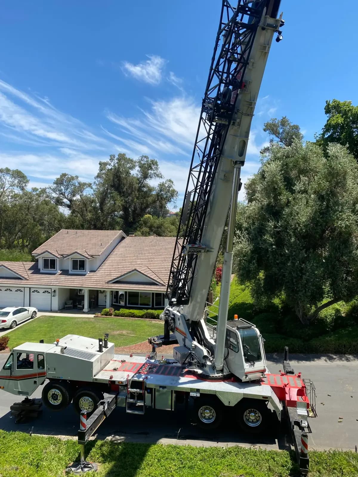 A boom lift set up on a driveway beside a tile-roofed house, boom raised toward the canopy