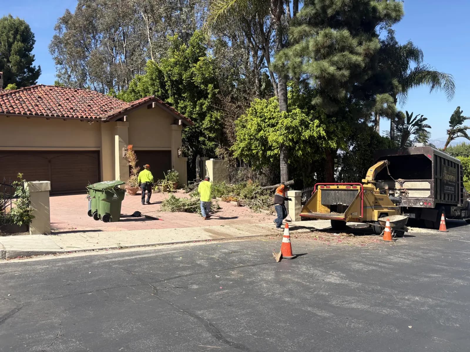 A chipper and wheeled green waste bins at a kerbside clean-up in front of a tile-roofed house