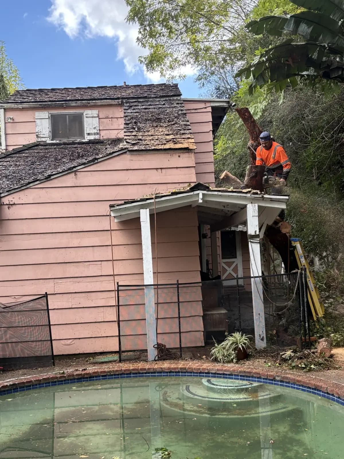 A crew member with a chainsaw cutting a failed limb clear of a roof eave