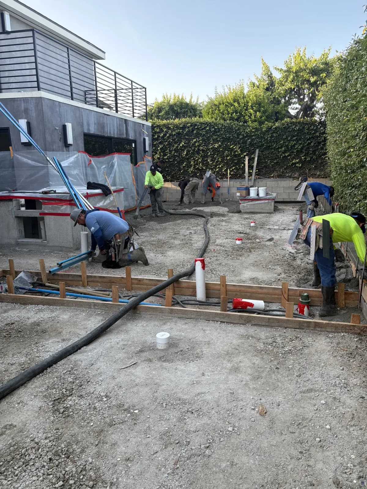 A hardscape crew setting timber forms, rebar and conduit across a prepared subgrade before a concrete pour