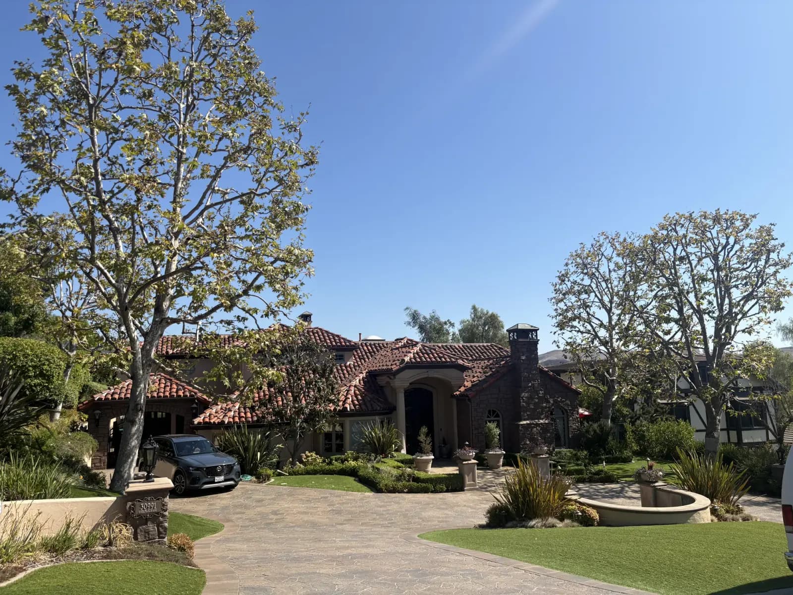 A Mediterranean-style estate with mature trees along the driveway and clipped hedging