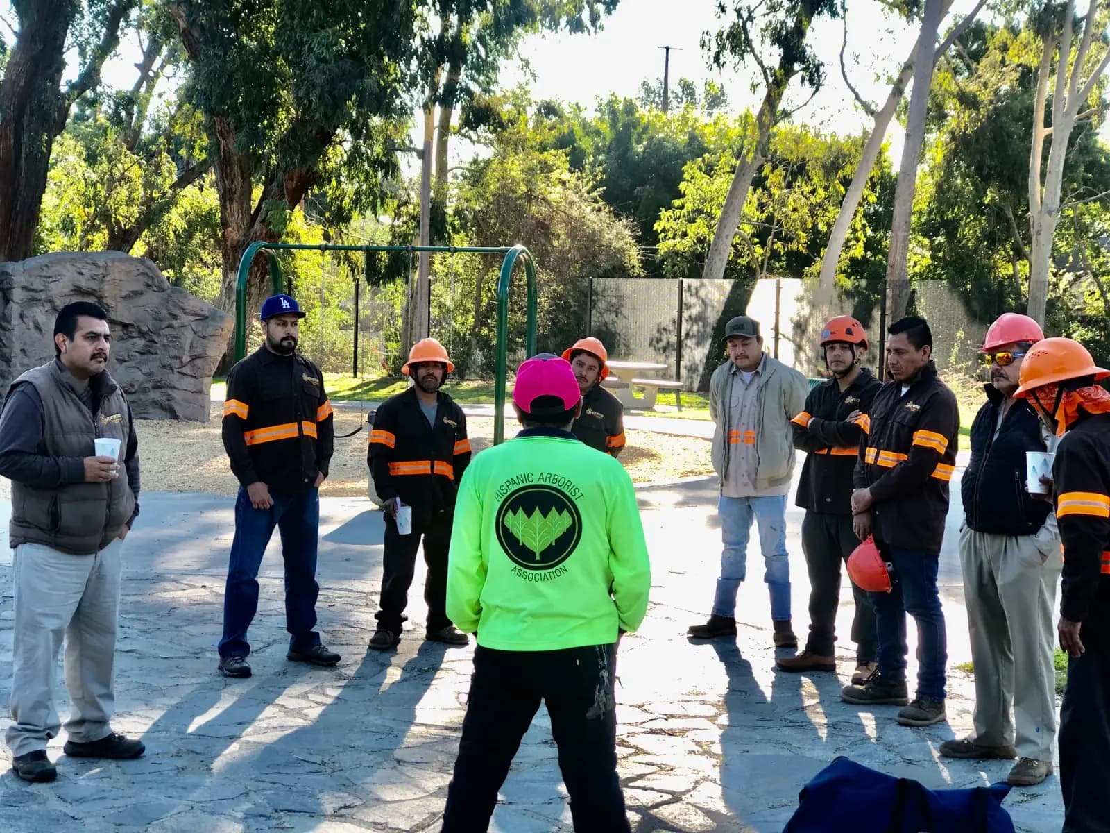 A tree crew standing in a circle outdoors for a safety meeting, most in helmets and hi-vis