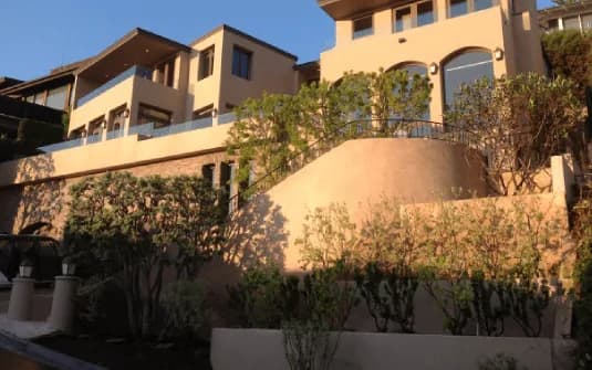 A terraced hillside estate at dusk, a wall-trained tree clipped into flat tiers against the stonework and shaped planting along the front steps