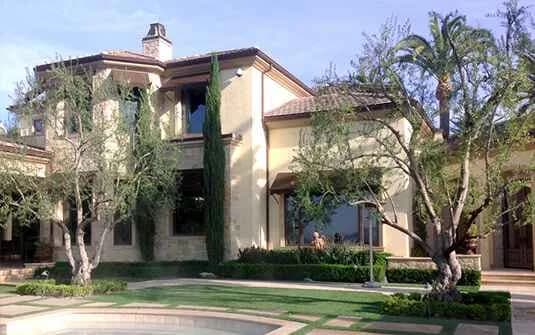 A two-story Mediterranean-style home fronted by mature olive trees, Italian cypress and clipped low hedging