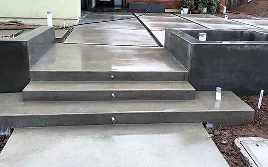 Newly poured concrete steps and landing with a concrete-faced planter wall, still under construction